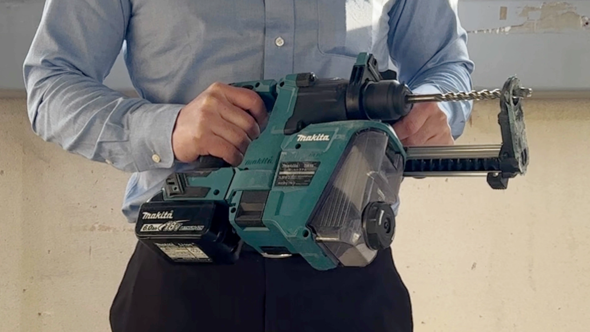 作業服姿の男性がマキタの集じんシステム付きハンマドリルを両手で構えている写真。実際のサイズ感と装着時のバランス確認用