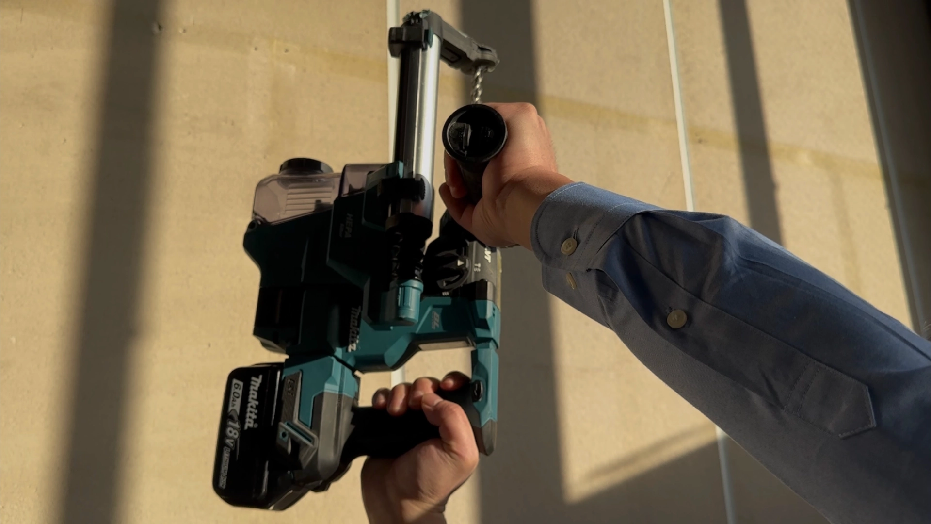 集じんシステムを装着したマキタハンマドリルを片手で垂直に持ち上げている様子。現場での取り回しや重量感のイメージ